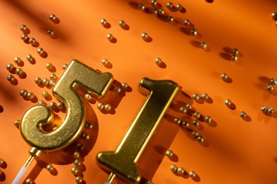 vibrant festive backdrop for 51st birthday, made of gold candles shaped like number fifty-one, placed on an orange background with sprinkles. versatile festive banner