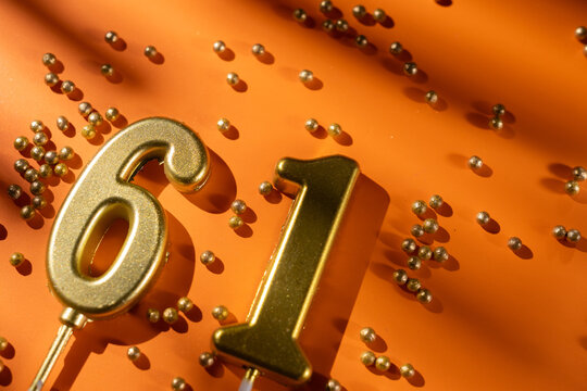 vibrant festive backdrop for 61st birthday, made of gold candles shaped like number sixty-one, placed on an orange background with sprinkles. versatile festive banner
