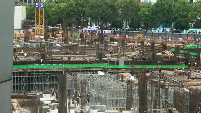Large urban construction site with workers assembling steel reinforcement and concrete formwork beside a city street. Infrastructure development and building project concept.