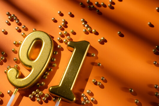 vibrant festive backdrop for 91st birthday, made of gold candles shaped like number ninety-one, placed on an orange background with sprinkles. versatile festive banner