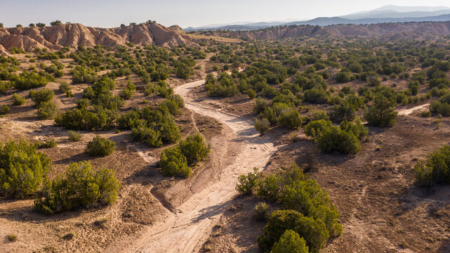 Aerial view of a dry sandy arroyo winding through a desert landscape dotted with juniper bushes in Taos County, New Mexico, United States.