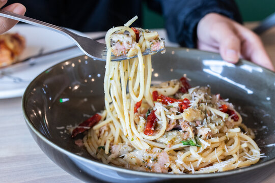 Fork lifting spaghetti aglio e olio with bacon dried chili and parmesan cheese from deep bowl. (
