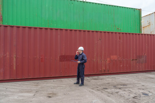 Construction worker inspecting cargo containers at shipping yard.