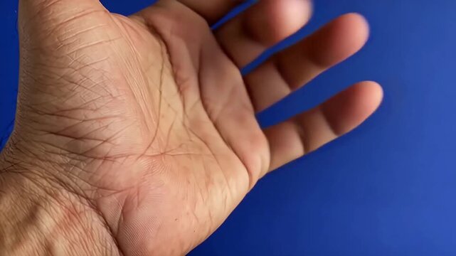 Hand with palm facing up, fingers poised to snap against a cobalt background, showcasing the gradual movement and positioning of fingers in a close-up frame