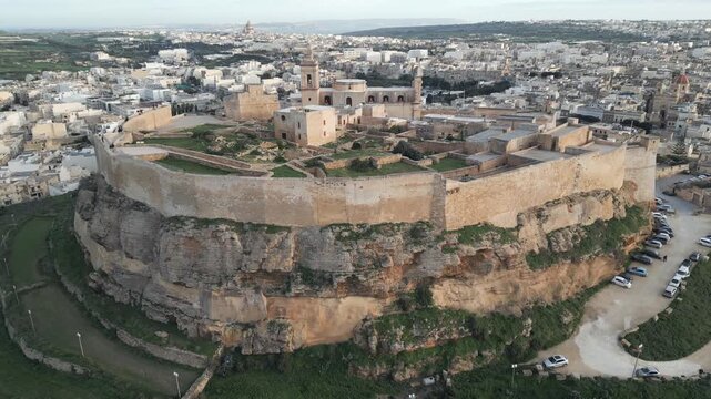 Aerial sideways tracking shot of the medieval Citadel in Victoria town illuminated by last sun rays, Gozo, Malta.