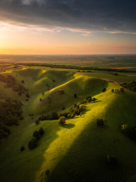 Aerial view of Zagajicka brda, featuring rolling green hills, scattered trees, and soft golden hour light under a dramatic sky in Vrsac, Vojvodina, Serbia.