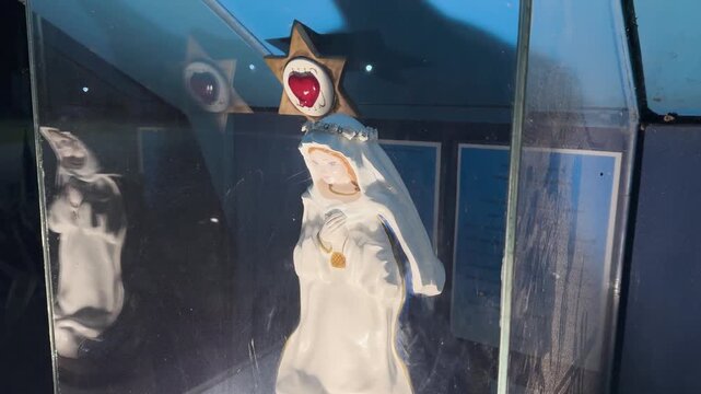 Close-up shot of a Virgin Mary statue inside a glass display, illuminated by soft, focused lighting in a Catholic shrine in Entre Rios, Argentina.