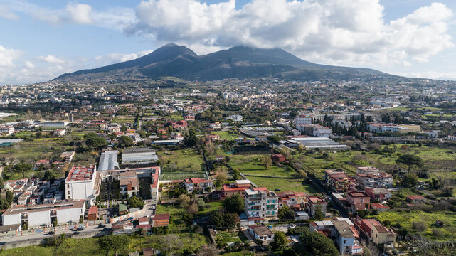 Aerial view of Mount Vesuvius towering over the residential neighborhoods, greenhouses, and green fields of the urban landscape in Naples, Campania, Italy.