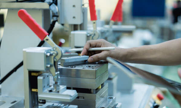Technician inspecting a precision metal fixture with a stylus and tablet in a manufacturing plant, representing quality control, engineering inspection, calibration, testing, and production accuracy.