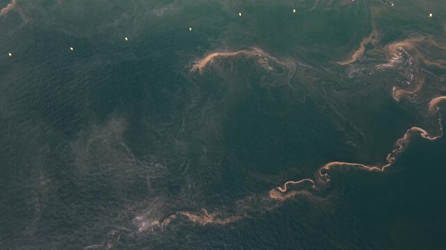 Aerial top down drone view of dark green open sea water with swirling currents and pale streaks of foam and pine pollen forming abstract patterns in Galicia Spain