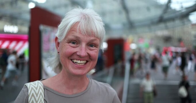Caucasian senior woman smiling on camera at bus station - Urban, travel and city lifestyle concept - Main focus on face - UGC content