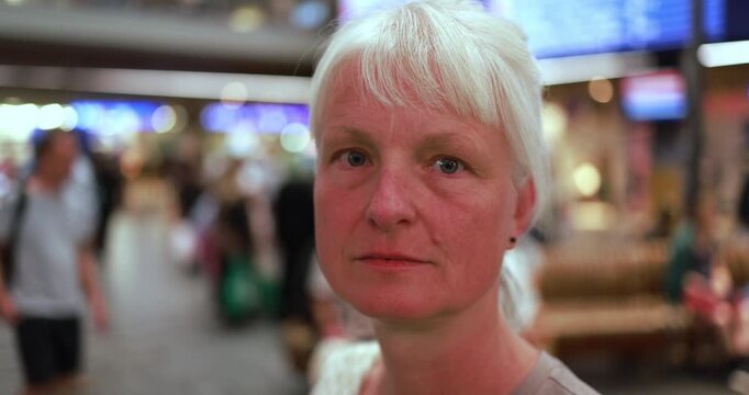 Caucasian senior woman looking at camera inside airport during evening time - Urban lifestyle and travel concept - UGC content - Main focus on face