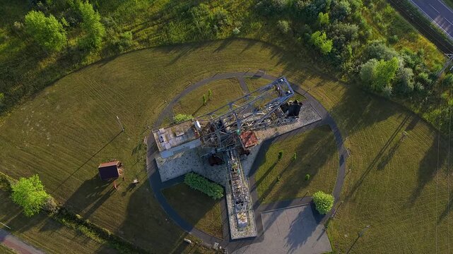 Top down aerial drone footage orbiting an old bucket wheel excavator monument, a relic from a coal mine, resting in a green park