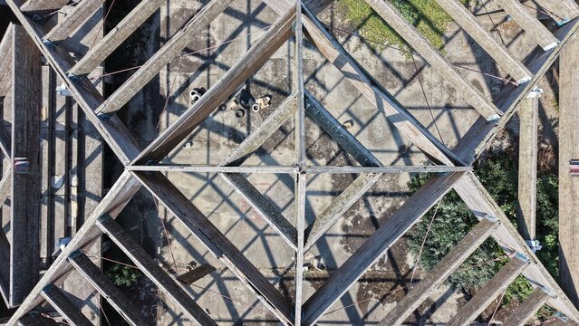 Aerial view of a geometric wooden roof structure with intersecting beams and shadows cast on the concrete ground in Pancevo, Serbia.