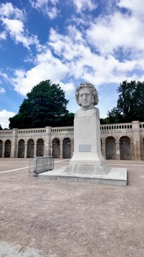Massive Sir Joseph Paxton bust stands on a wide plaza before the arched Crystal Palace Park Terrace under a blue sky with clouds. vertical video