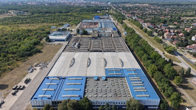Aerial view of the industrial facility in Severna zona with large blue and grey rooftops, surrounding green trees, and nearby roads in Pancevo, Serbia.