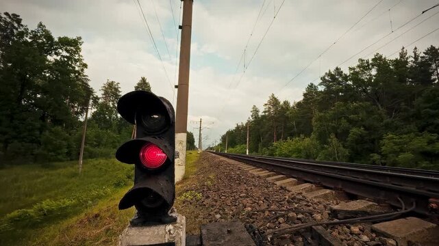 A railway traffic light with a red signal against the background of rails and sleepers in an open area. The concept of prohibition and restriction of movement 