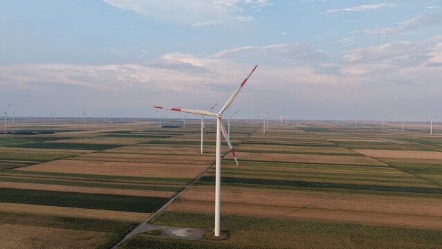 Aerial view of a wind turbine standing in a vast agricultural field with rows of crops under a soft sky in Crepaja, Vojvodina, Serbia.