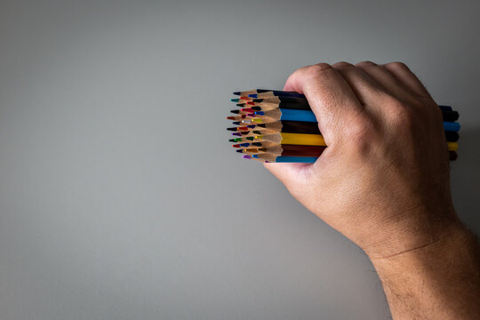 Hand Holding Colorful Pencils Against a Plain Gray Background