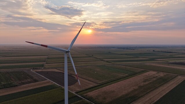Aerial view of a wind turbine standing in vast agricultural fields during a golden sunset in Crepaja, Vojvodina, Serbia.