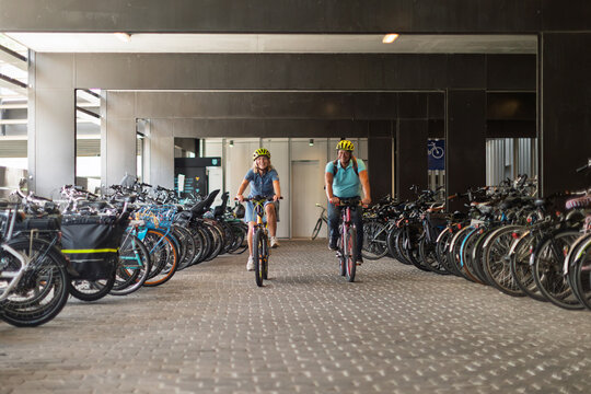 Couple cycling with helmets through a bicycle parking garage
