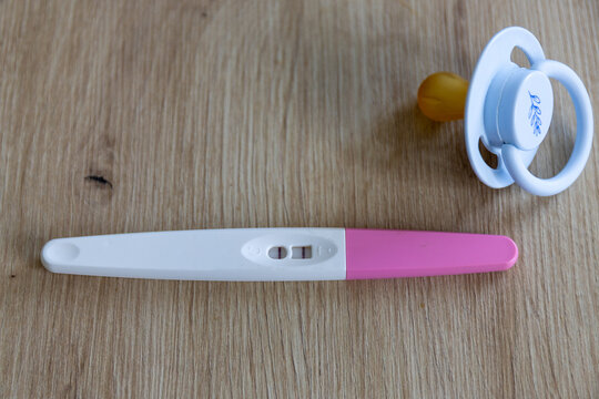 Positive pregnancy test with two lines lying next to a white baby pacifier on a wooden background.