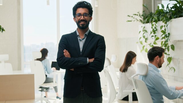 Confident Arabian Indian business man CEO smiling looking at camera indoor office team boss employer executive manager posing corporate portrait arms folded company leader career workplace businessman