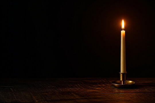 A single lit taper candle in a plain brass holder standing on a dark