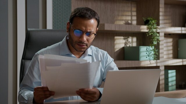 Angry frustrated Indian American business man throwing papers desk stressed worker with laptop tired unhappy male businessman office employee deadline paperwork problem burnout hate trouble hard work