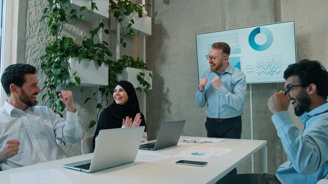 Cheering happy diverse multiethnic business team celebrating success startup indoor office Arabian businessmen muslim businesswoman victory work laptop partners teamwork colleagues win deal boardroom