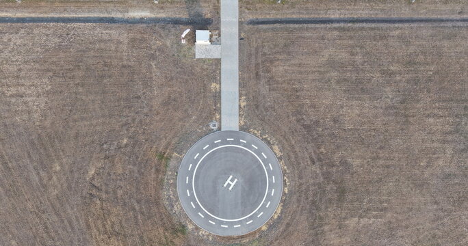 Aerial view of a helipad with an H marking in the Severna zona industrial area, surrounded by dry fields and a concrete access path in Pancevo, Serbia.
