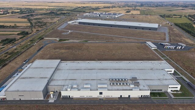 Aerial view of the Severna zona industrial complex featuring large warehouse buildings with flat roofs, a parking area with trucks, and surrounding open fields in Pancevo, Serbia.