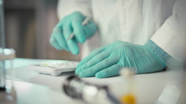 Laboratory worker carefully inputs numbers into calculator to process data at his lab workstation, illustrating precise analytical routine scientists follow in modern research laboratory environment
