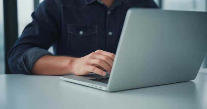 Young man in denim shirt typing on laptop during casual work session