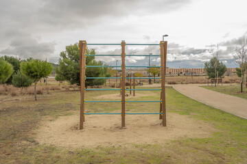 Obraz premium Wooden outdoor exercise structure with green horizontal bars in a park under an overcast cloudy sky.
