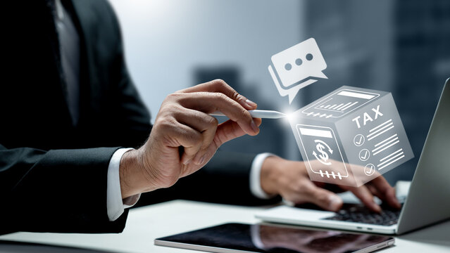 A businessman in a suit uses a laptop while interacting with a futuristic holographic 3D tax icon and financial charts. Concept of a Tax Consultant