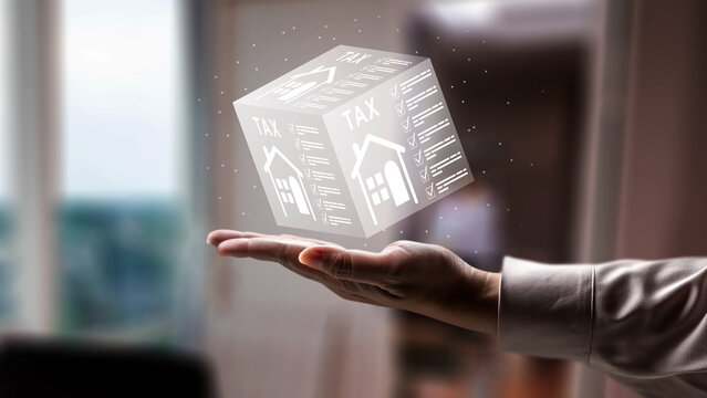 Closeup of a hand holding a glowing holographic cube featuring a house icon and the word TAX, representing digital property tax solutions and home financial planning. Concept of house and property tax