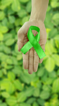 Hands holding a green awareness ribbon, symbolizing mental health or environmental support, against blurred green foliage. Concept of World Mental Health Day