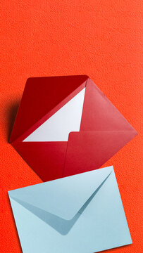An open red envelope with a blank white card and a closed light blue envelope on a vibrant textured orange background. Concept of World Post Day