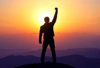 Fototapeta premium Silhouette of a triumphant person standing on a mountain peak at sunset with raised fist
