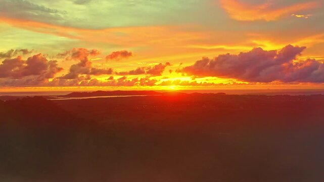 Aerial view of Soft morning fog drifts gently through the valley, wrapping the hills in a silver veil. The horizon glows with golden light, reflecting hues of pink and orange across the clouds above