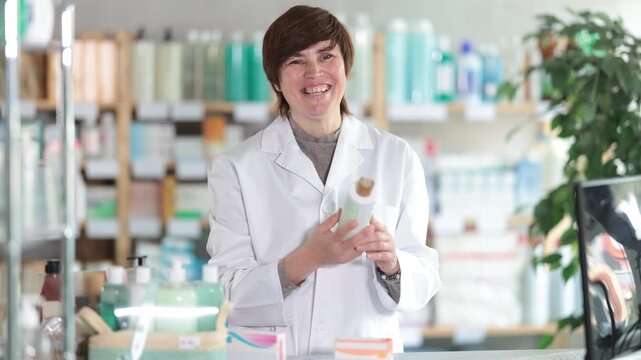 Female pharmacist in white coat standing at counter in pharmacy, recommending ointment to customer, offering expert advice and assistance with over-the-counter treatment