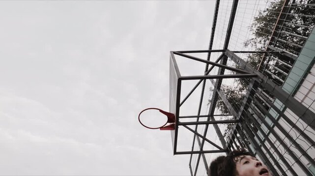 Close up of basketball player dunking on outdoor court under overcast sky
