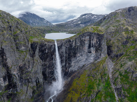 Aerial view of Mardalsfossen waterfall cascading down a steep rocky cliff face from a mountain lake under a cloudy sky in Eikesdalen, More og Romsdal, Norway.