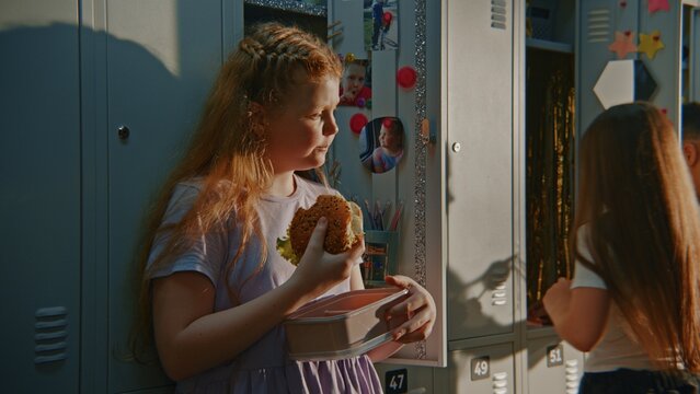 Young Girl Standing Beside Personalized Locker Decorated with Photos, Colorful Magnets While Eating Homemade Sandwich. School Identity, Personal Space, Childhood Independence, Everyday Campus Life.