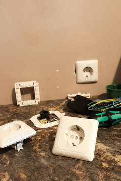Electrical sockets installation and repair process in a room. Vertical close up of white power outlets, disassembled plastic frames, wires, and tools lying on a kitchen countertop during home renovati