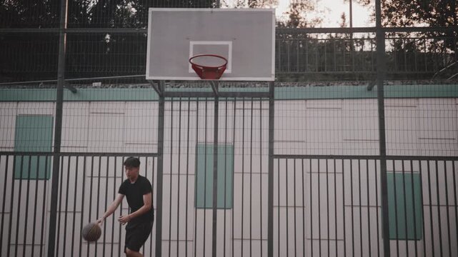 Young man playing basketball on outdoor court shooting ball at hoop