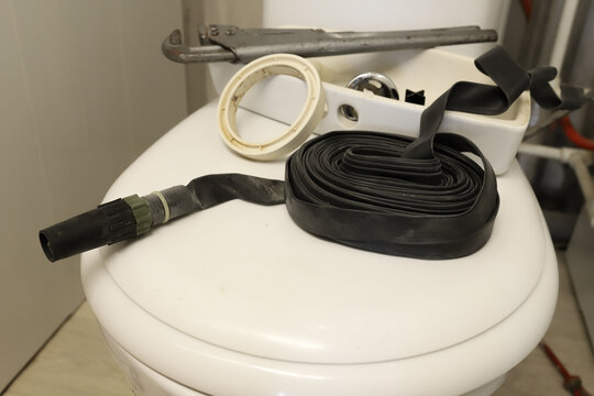 Plumbing tools and replacement parts lying on a white toilet lid during a bathroom repair process. Close up horizontal portrait of rubber tape, wrench, sealant, and details for fixing a home water lea
