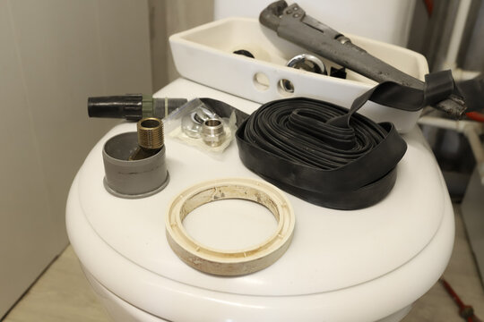 Plumbing tools and replacement parts lying on a white toilet lid during a bathroom repair process. Close up horizontal portrait of rubber tape, wrench, sealant, and details for fixing a home water lea