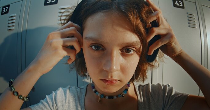 Portrait of Teenage Girl Wearing Headphones Looking Directly While Standing Near School Lockers Bathed in Warm Golden Hour Light. Confident Expression, Youth Culture, Modern Gen Z Student Lifestyle.
